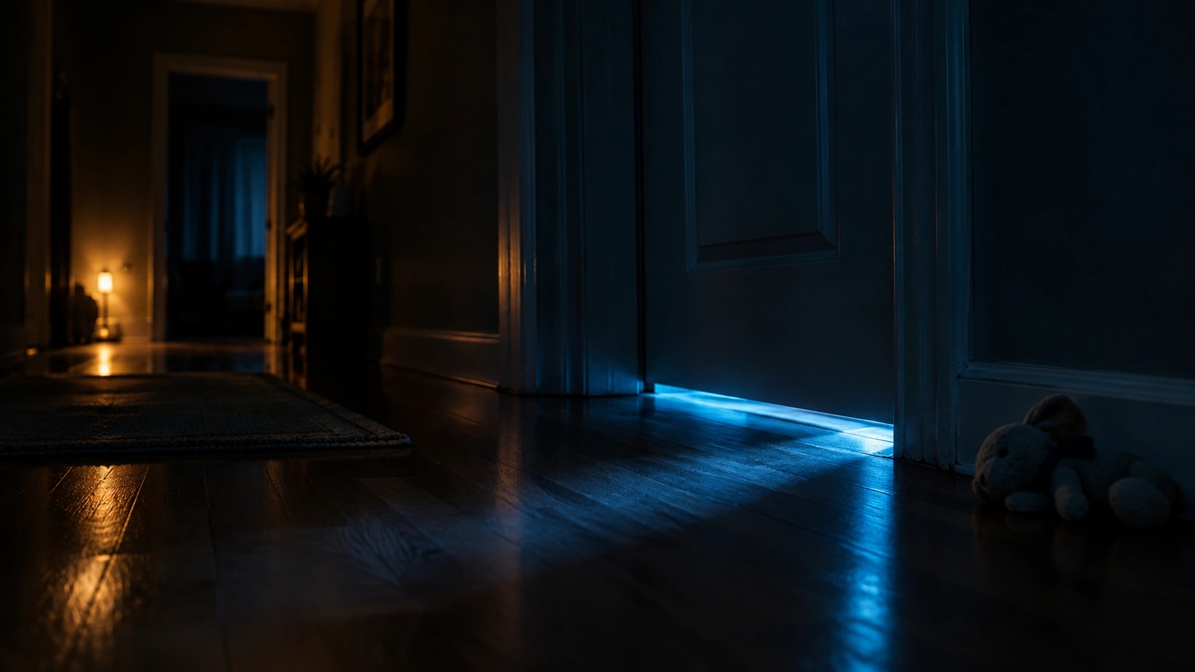 Phone screen glow leaking from under a closed bedroom door at night